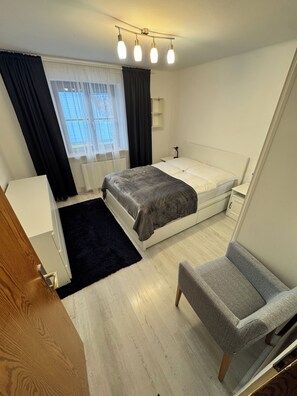 Une chambre à coucher avec un lit, une table de chevet, une chaise et une fenêtre avec des rideaux.