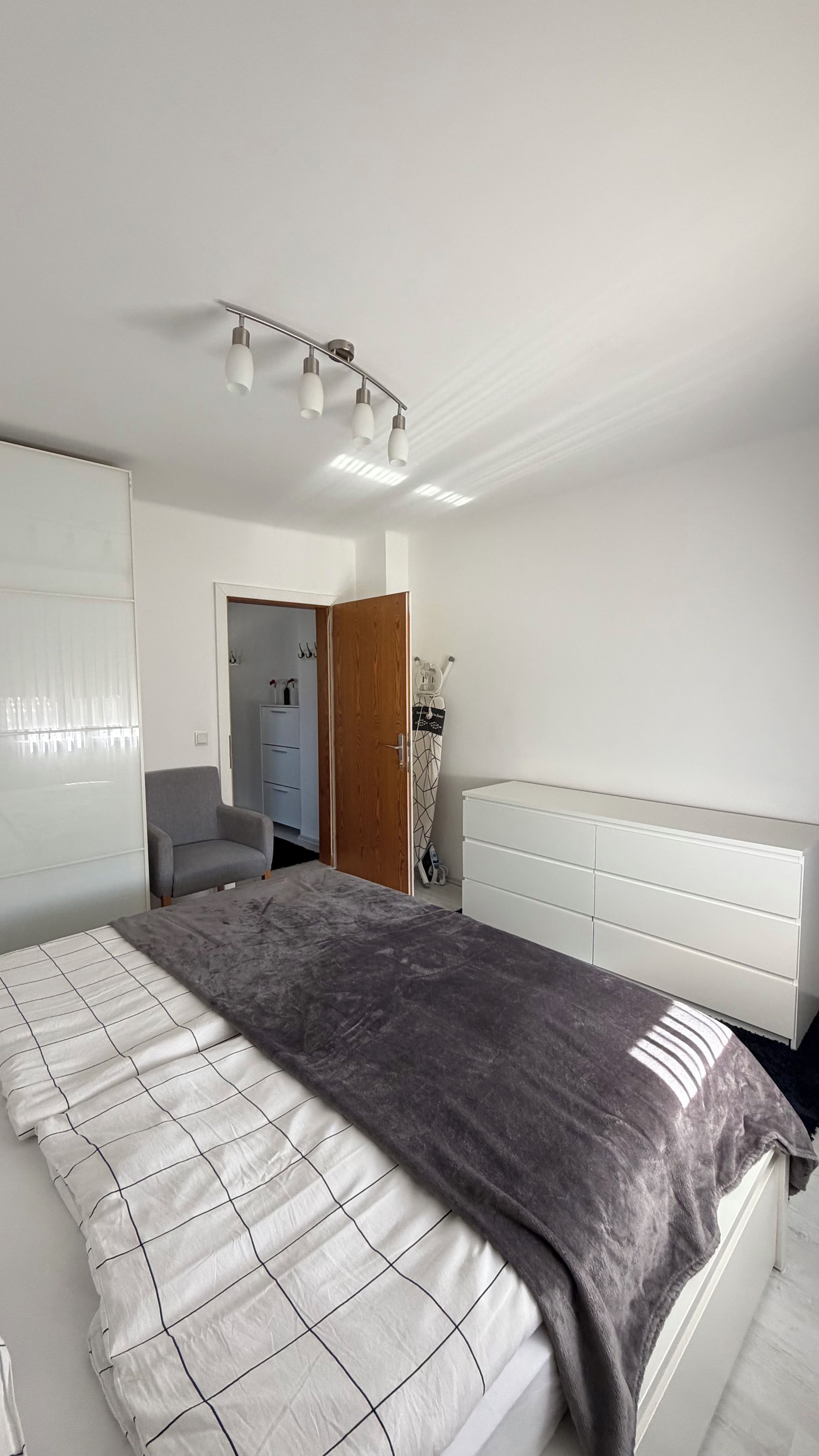 A bedroom with a bed, a wardrobe, a desk, and a door leading to another room.