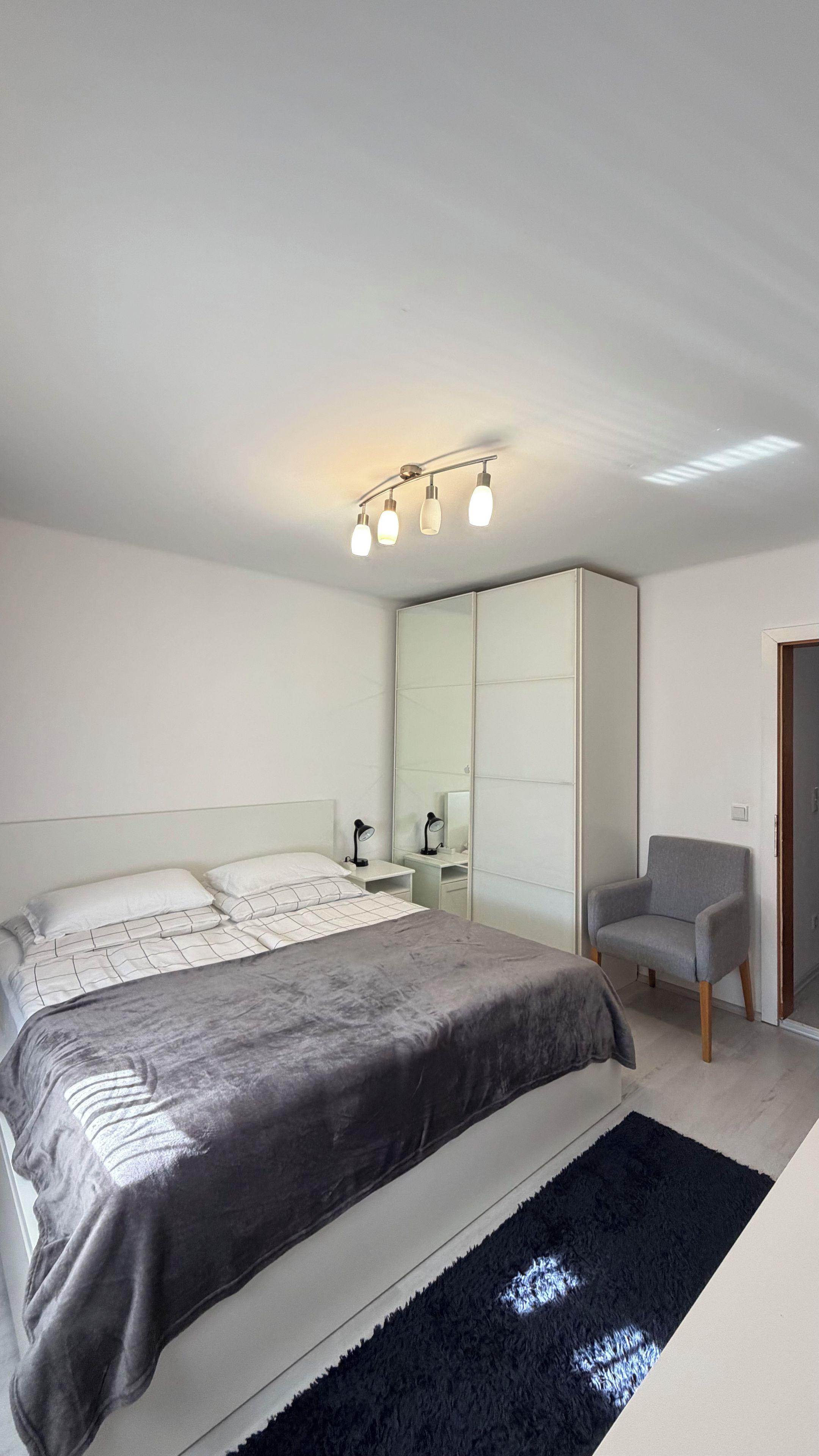 Een moderne slaapkamer met een groot bed, een stoel, een spiegel en een kledingkast.