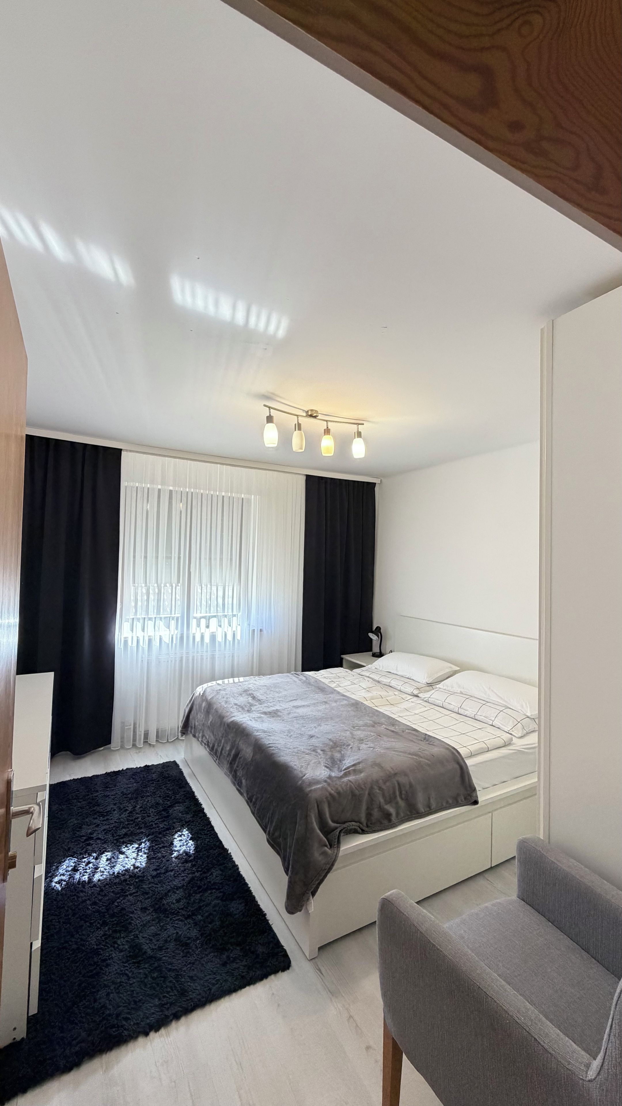 A bedroom with a bed, a chair, a desk, and a window with curtains.