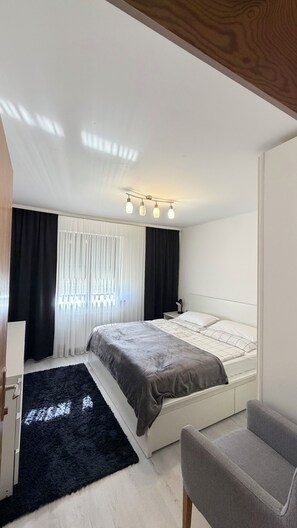 Une chambre à coucher avec un lit, une chaise, un bureau et une fenêtre avec des rideaux.