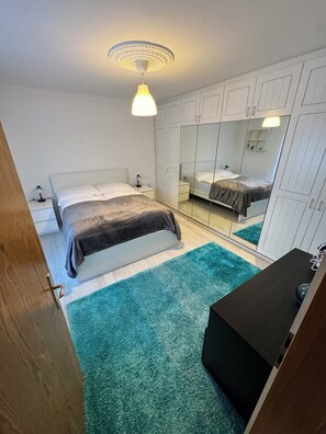 Une chambre à coucher comprenant un lit, une table de chevet, une commode, un miroir et un luminaire au plafond.
