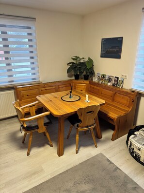 Un coin repas avec une table en bois et des bancs, une plante en pot et une affiche accrochée au mur.