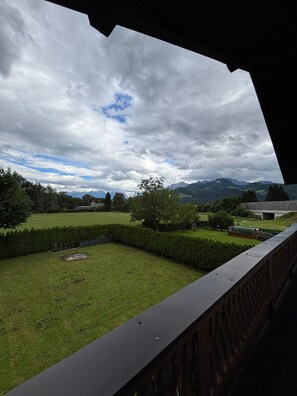 A view from a balcony overlooking a well-maintained lawn, a building with a modern design, and distant mountains under a cloudy sky. - Cozy 2-room apartment with mountain views (Oberalm)