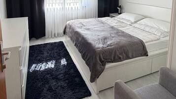 A modern bedroom with two beds, a desk, and a chair.