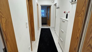 Un couloir étroit avec des portes en bois, un tapis noir et un mur blanc éclairé par un luminaire au plafond.