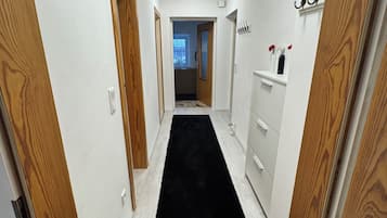 Een smalle gang met houten deuren, een zwart tapijt en een witte muur met plafondlamp.