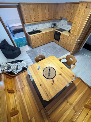 A compact kitchen with wooden cabinets, a small dining table, and a bean bag chair. - Cozy 2-room apartment with mountain views (Oberalm)