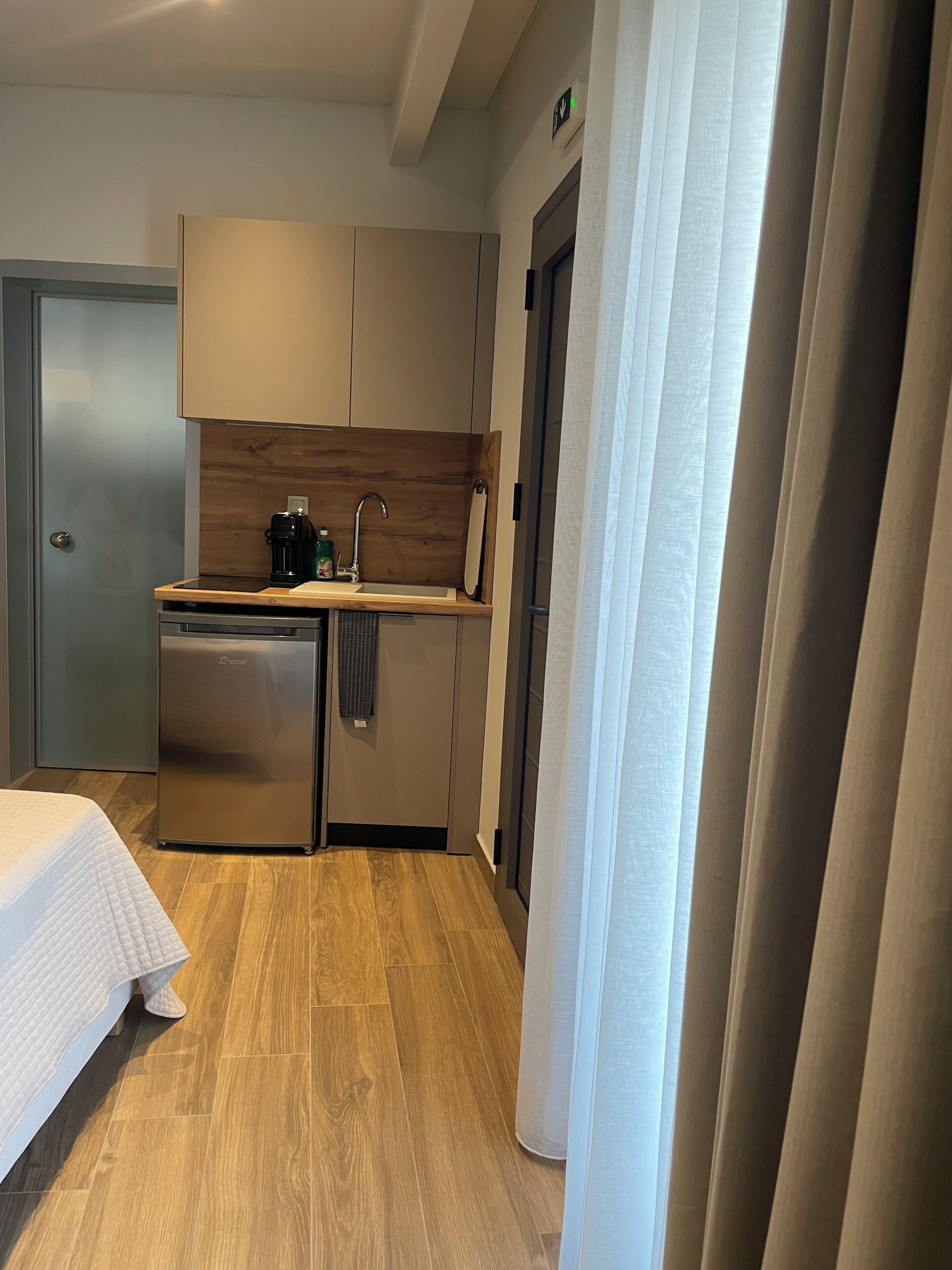A compact hotel room with a kitchenette, a bed, and a door leading to another room.