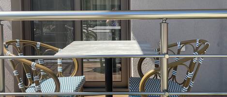 A balcony with a table and chairs, a glass door, and a view of the street.