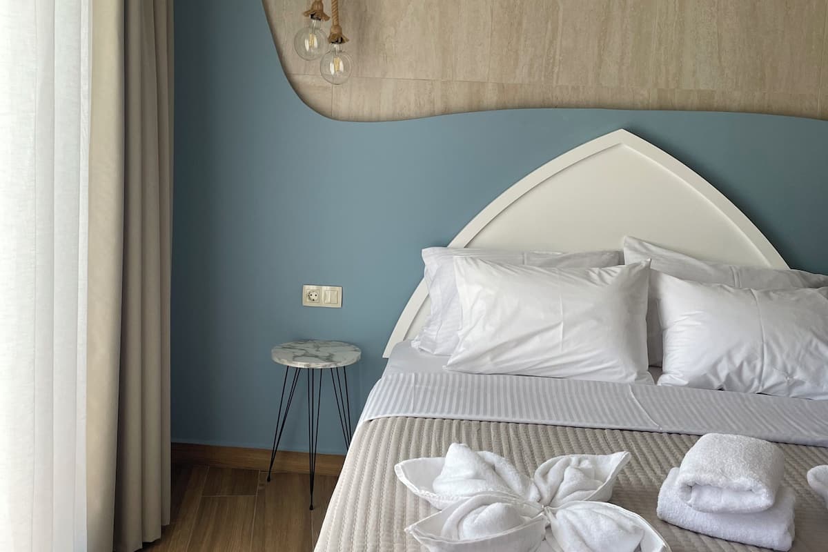 Una habitación de hotel con cama, almohadas, una mesita de noche, una lámpara y un aplique de pared.