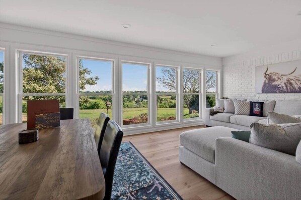A room with a large window, a wooden table, a sofa, and a mounted animal head.