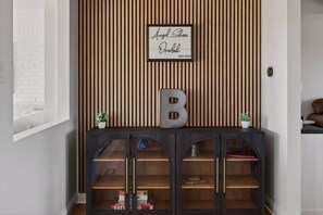 A room with a wooden slat wall, a framed sign, a cabinet with glass doors, and a large letter 'B' on top.