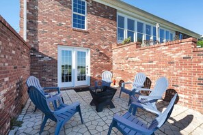 A brick patio with Adirondack chairs, a fire pit, and a white door.