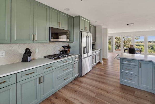 A modern kitchen with light green cabinets, stainless steel appliances, and a large island.