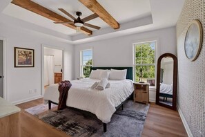Quarto com cama, mesa de cabeceira, espelho e janela com vista para o verde.