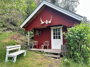 A red cabin with a porch, a bench, and a deer head decoration.