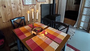 Un interior de madera con una mesa dispuesta para comer, una estufa negra y documentos enmarcados en la pared.