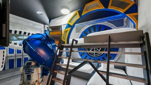 Ein Zimmer mit Etagenbetten, einer Wand mit Weltraum-Motiven und einer großen, radartigen Struktur.