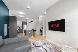 Una sala de estar moderna con un sofá gris, una mesa de centro y un televisor montado en la pared mostrando 'NETFLIX'.