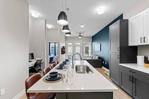 Eine moderne Küche mit Kochinsel, Essbereich mit Stühlen, integriertem Backofen und großem Fenster.