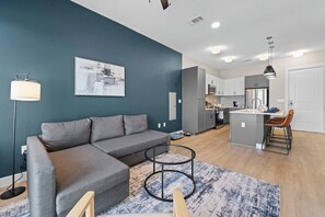 Uma sala de estar moderna com um sofá cinza, uma mesa de centro redonda pequena e um tapete azul estampado.