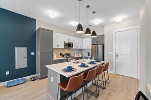 Una cocina moderna con una isla central, electrodomésticos de acero inoxidable e iluminación colgante.