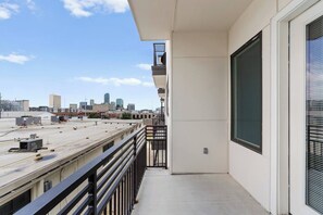Un balcon avec vue sur la ville, une rambarde en métal et la façade d’un immeuble avec une fenêtre et une porte.
