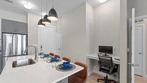 A modern kitchen with a central island, dining chairs, a built-in oven, and a computer desk with a chair.