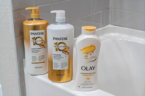 Kolme Pantene- ja Olay-tuotepulloa kylpyhuoneen tasolla.