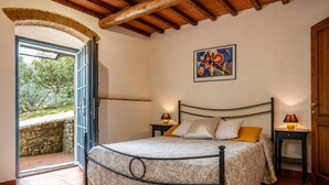 Ein Schlafzimmer mit einem Bett, zwei Nachttischen, einem Gemälde und einer offenen Tür zu einer Steinwand.