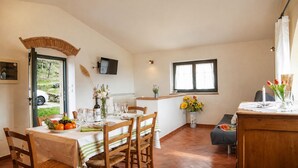 Ein Essbereich mit Tisch für vier Personen, Stühlen, einem an der Wand befestigten Fernseher und einem Fenster mit Vorhängen.
