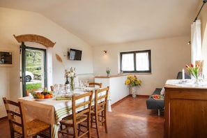 Un coin repas avec une table dressée pour quatre personnes, des chaises, un téléviseur fixé au mur et une fenêtre avec des rideaux.