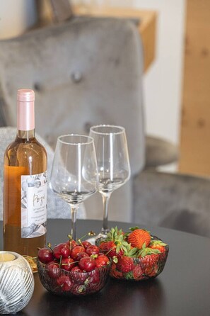 Eine Weinflasche, zwei leere Gläser und eine Schale mit Kirschen und Erdbeeren auf einem Tisch.