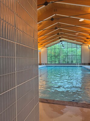 Ein Innenpool mit einer Fliesenwand und einer Holzbalkendecke.