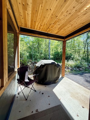 Un espace extérieur abrité avec des sièges et une chaise pliante, ainsi qu’un barbecue couvert.