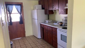 A compact kitchen with a refrigerator, stove, microwave, and wooden cabinets. - Budgetel Inn & Suites (Yuma)