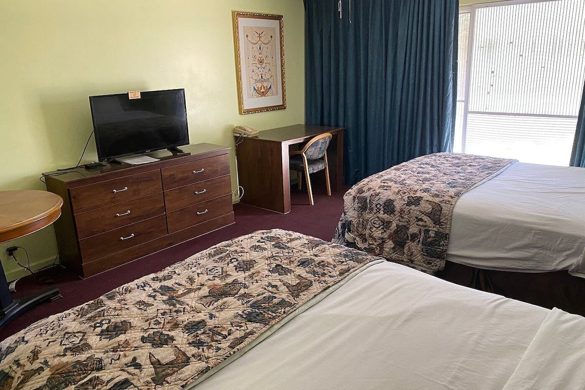 Una habitación de hotel con dos camas, un escritorio, un aparador, un televisor y un cuadro en la pared.