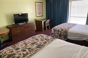 Una habitación de hotel con dos camas, un escritorio, un aparador, un televisor y un cuadro en la pared.
