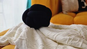 A bed with a white blanket and a black pillow, a yellow cushion, and a teal curtain in a room with a white wall. - Stylish High-Rise Retreat, Skyline Views, Gym & Rooftop in Kilimani (Nairobi)