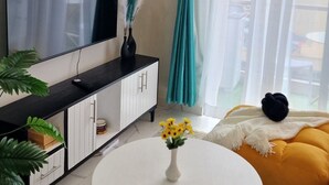 A modern living room with a flat-screen TV, a round white table with a vase of flowers, a yellow sofa, and teal curtains. - Stylish High-Rise Retreat, Skyline Views, Gym & Rooftop in Kilimani (Nairobi)