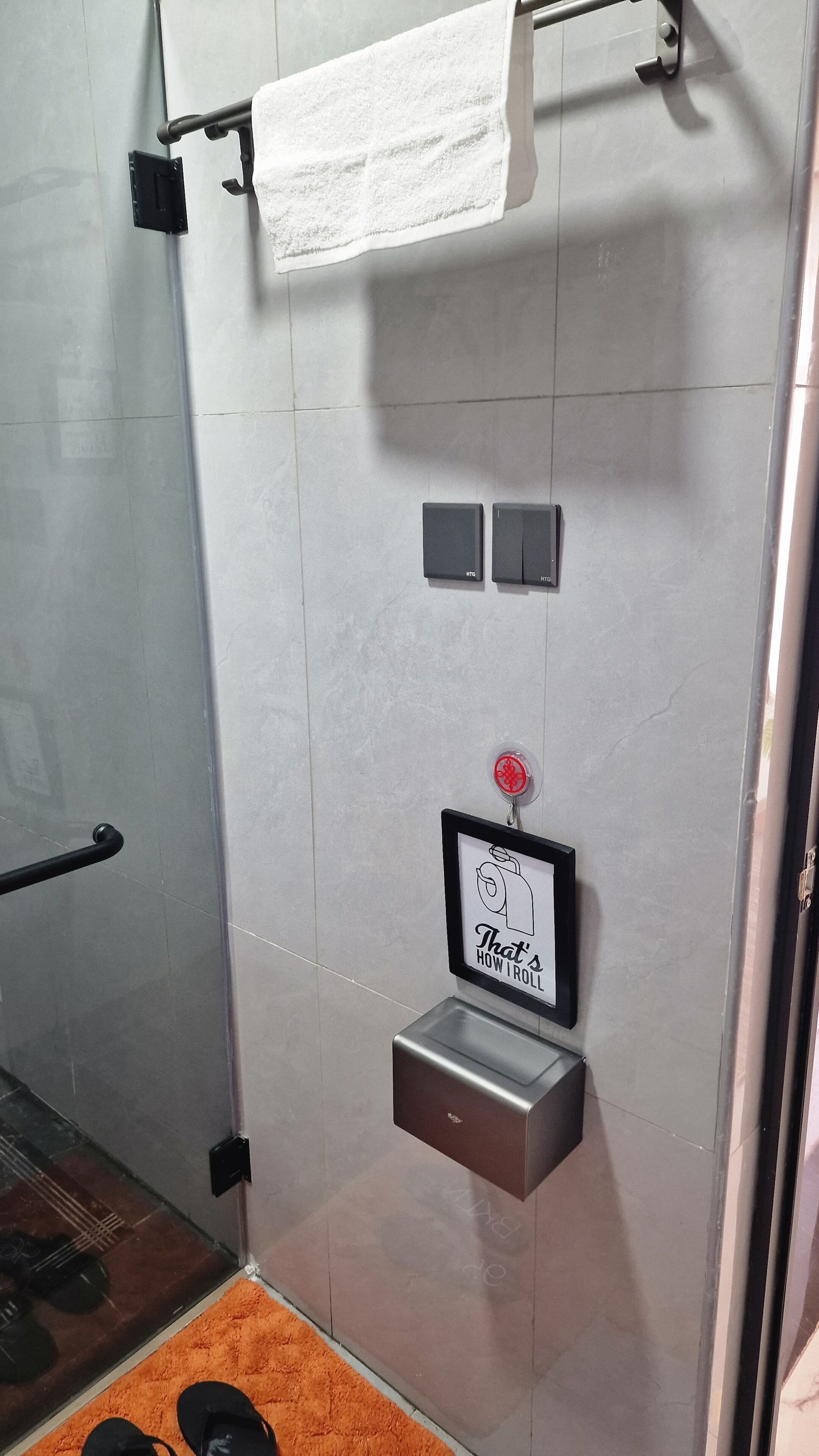 Une salle de bain équipée d’un porte-serviettes, d’un sèche-mains, d’un distributeur de savon et d’une affiche encadrée.