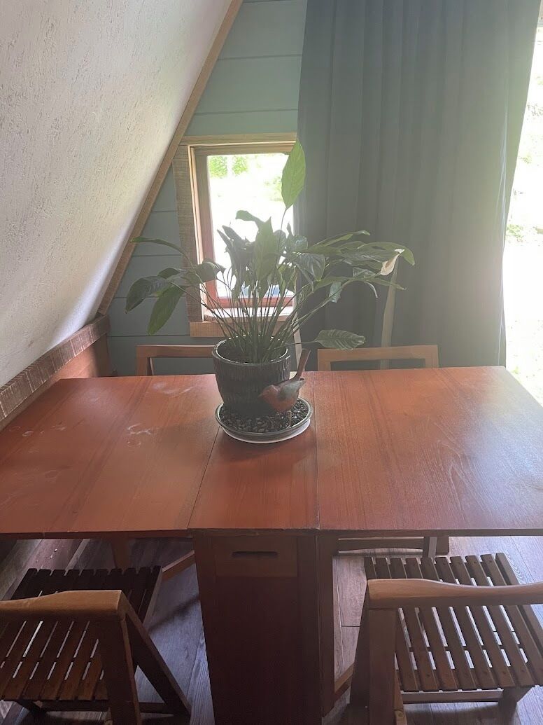 Une table à manger en bois, avec des chaises, une plante en pot et une fenêtre avec des rideaux.