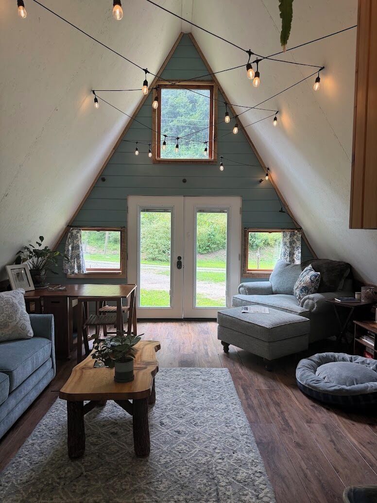 A cozy loft-style room with a sloped ceiling, a dining area, a sofa, a small table, and a pet bed.