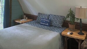 A cozy bedroom with a sloped ceiling, a bed with a patterned pillow, a bedside lamp, a small table, and a potted plant. - A-Frame Cabin -The Get Away #1 (Diana)