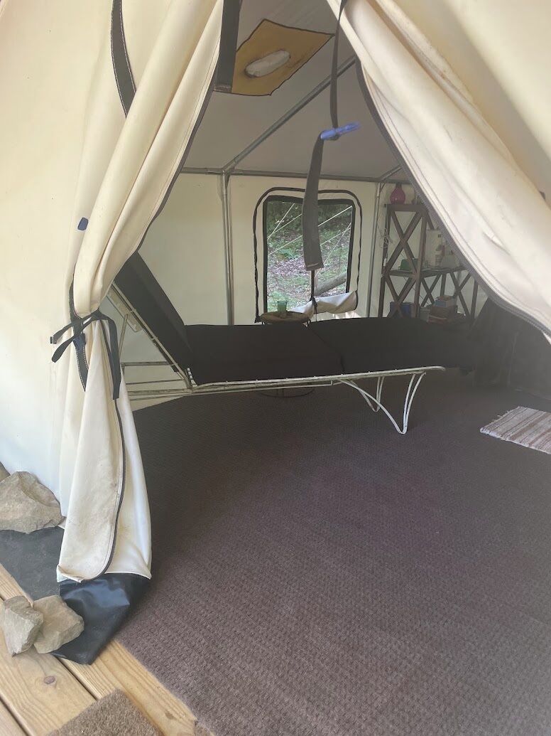 A tent with a bed inside, a window, and a small table with a chair.