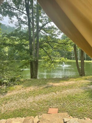 A view of a lake with trees and a fountain, viewed from under a structure. - Glamping tent overlooking pond (Diana)