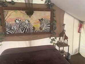 A tent with a bed, a painting of zebras, a giraffe sculpture, and hanging plants. - Glamping tent overlooking pond (Diana)