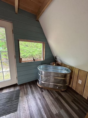 Ein Zimmer mit Fenster, einem Metallwaschbecken, Holzboden und einer Tür.
