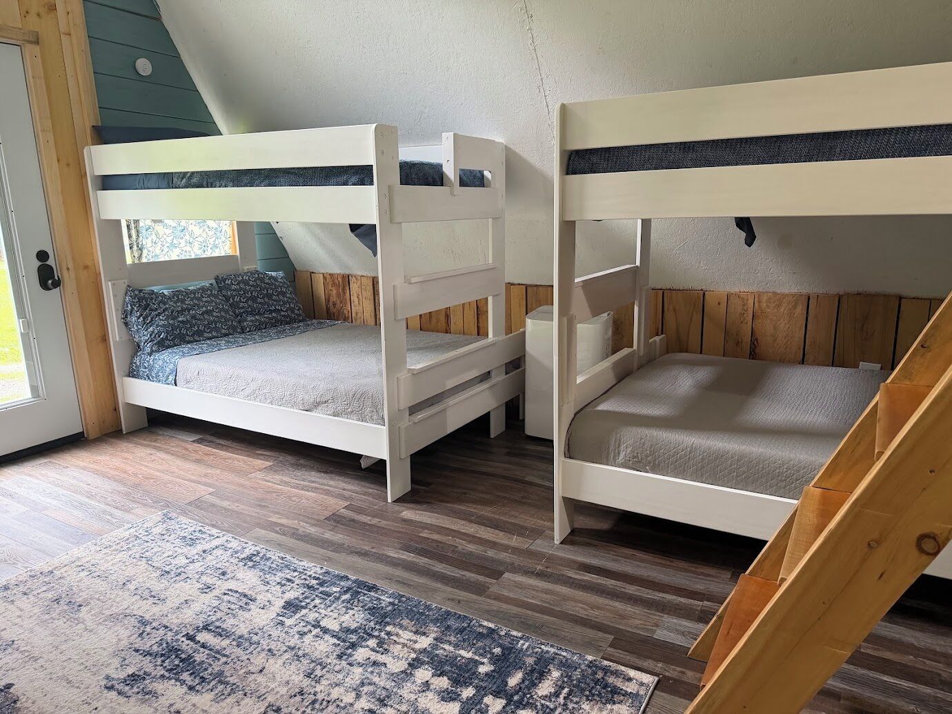 A room with two bunk beds, a wooden floor, a patterned rug, and a door with a window.